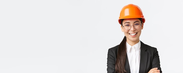 Il leader sorridente del team asiatico capo ingegnere in casco di sicurezza e tuta incrocia le braccia sorridendo fiducioso felice alla telecamera introduce l'impresa in piedi su sfondo bianco