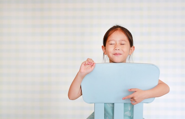 La piccola ragazza prescolare sorridente del bambino asiatico in una stanza di asilo posa sulla sedia di plastica del bambino