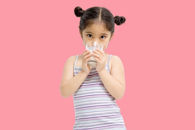 Smiling little Asian girl drinking milk isolated on pink background