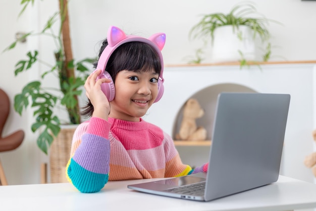 웃고 있는 어린 아시아 소녀는 코로나바이러스 동안 격리된 동안 사회적 거리를 두고 노트북을 사용하여 교사와 화상 통화를 합니다.