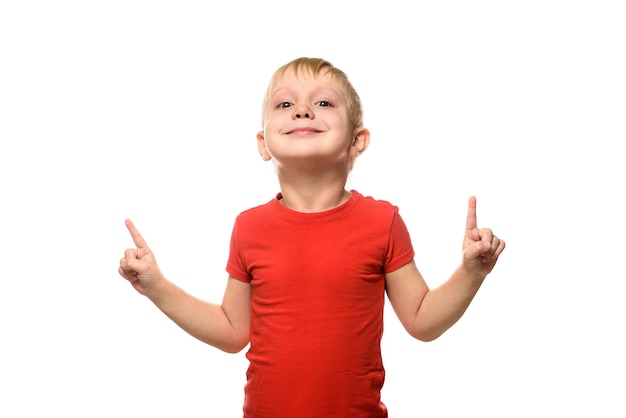 Smiling little blond boy in a red T-shirt is standing and pointing with his index fingers upwards