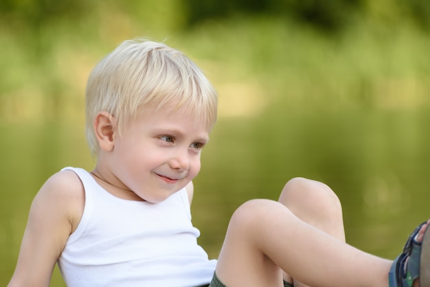 Piccolo ragazzo biondo sorridente che si siede all'aperto