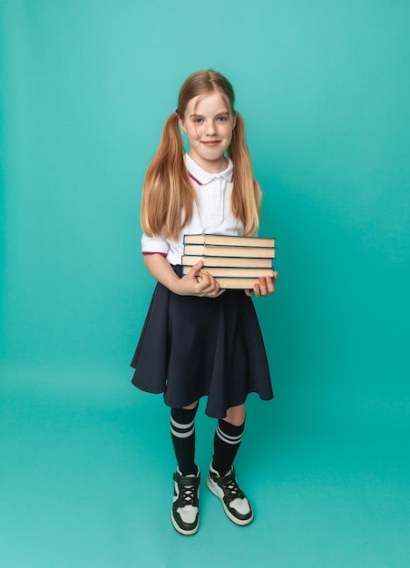 Smiling little blonde girl 1012 years old in school uniform with backpack holding books isolated on pastel blue background studio portrait The concept of children's lifestyle Education at school