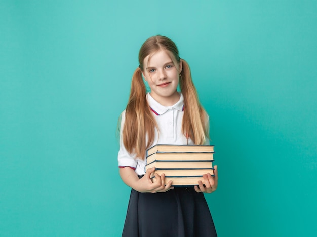 파스텔 블루 배경 스튜디오 초상화에 고립된 책을 들고 배낭을 메고 교복을 입은 1012세의 웃고 있는 어린 금발 소녀 학교에서의 어린이 생활 교육의 개념