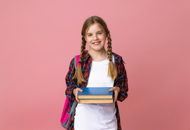 Smiling little blonde girl 1012 years old in school uniform with backpack holding books isolated on pastel pink background studio portrait The concept of children's lifestyle Education at school