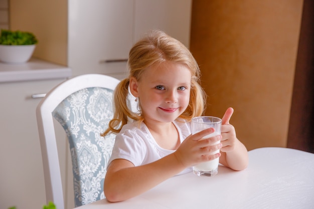 Smiling little blonde girl drinking milk in the kitchen