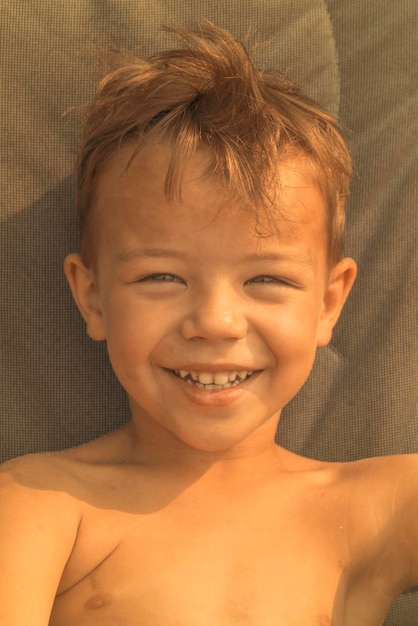 Smiling little boy brunette lays on a chair closeup sunny