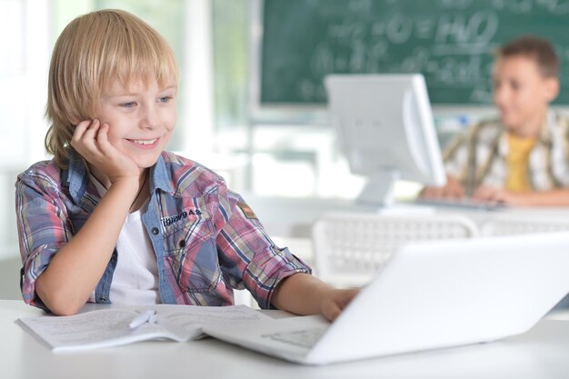 Smiling little boy in the classroom, his classmate on background