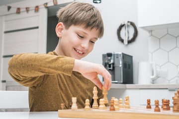 Premium Photo  Smiling little boy joying playing chess on wooden