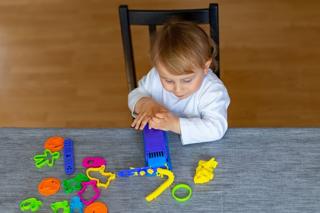 Smiling little boy molds from colored plasticine on table