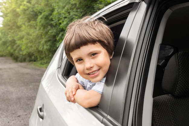 Smiling little boy rides in car looks out the open window have fun enjoying auto ride outdoors in