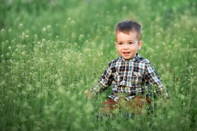 写真 春の日に花の咲く草原に座っている笑顔の小さな男の子屋外の美しい子供の肖像画