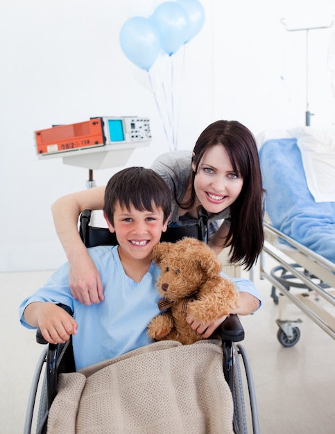 Smiling little boy sitting on wheelchair and his mother