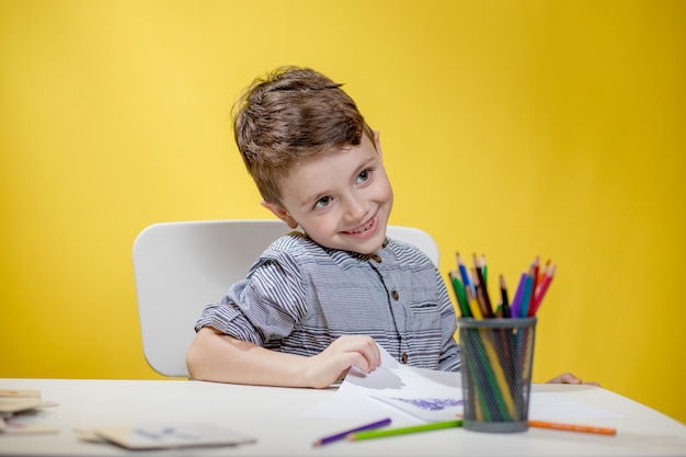 Smiling little boy at the table draw with crayons