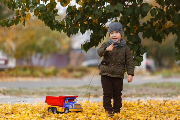 秋に屋外でおもちゃの車で遊んで遊んでいる少年の笑顔。幸せな子供時代のコンセプト。面白い子の肖像