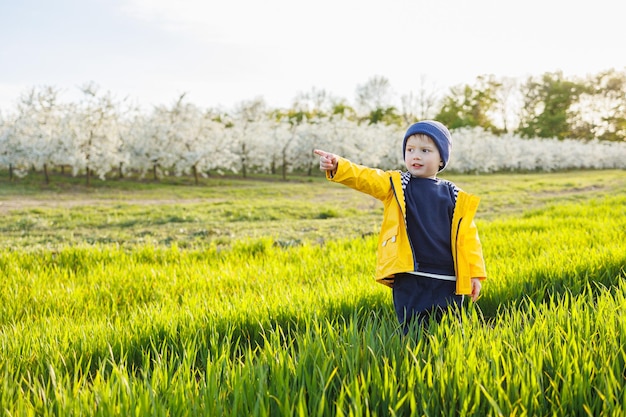 黄色いジャケットを着た笑顔の小さな男の子が開いた庭を走っています幸せな子供時代