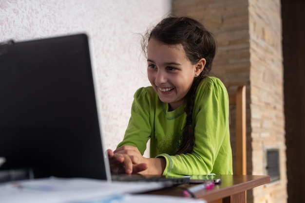 Photo smiling little caucasian girl in headphones have video call distant class with teacher using laptop, happy small child wave greeting with tutor, study online on computer, homeschooling concept.