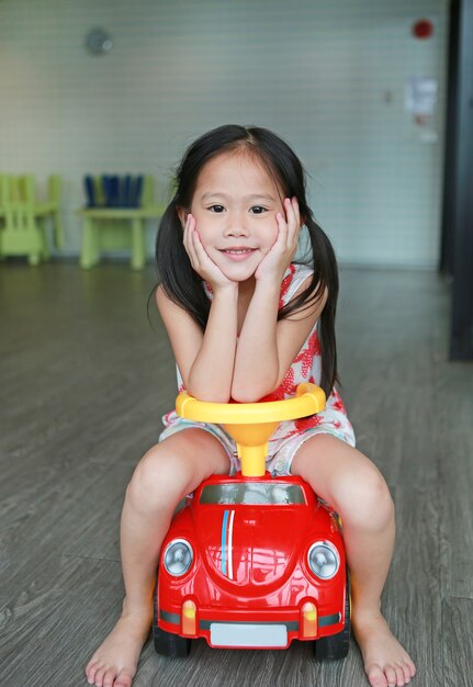 プレイルームで小さな車に乗って笑顔の小さな子供女の子。