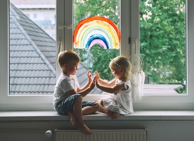 Smiling little children on background of painting rainbow on window