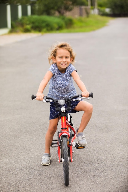 The smiling little girl on a bicycle stands in the middle of the street