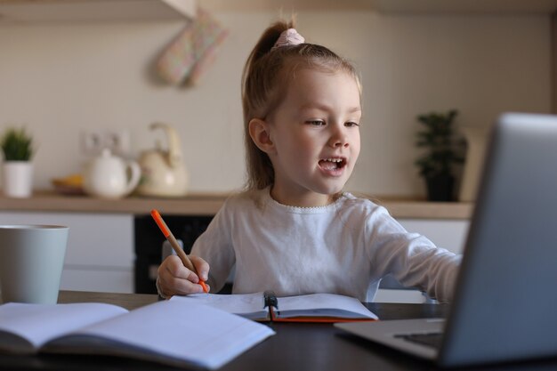 家でラップトップを使用してオンラインで小さな女の子の手書きの勉強を笑顔、かわいい幸せな小さな子供はPCでインターネットのWebレッスンまたはクラスを受講します。