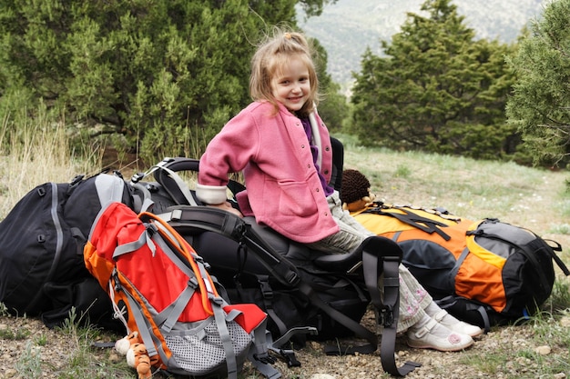 Smiling little girl hiker sitting on a backpack