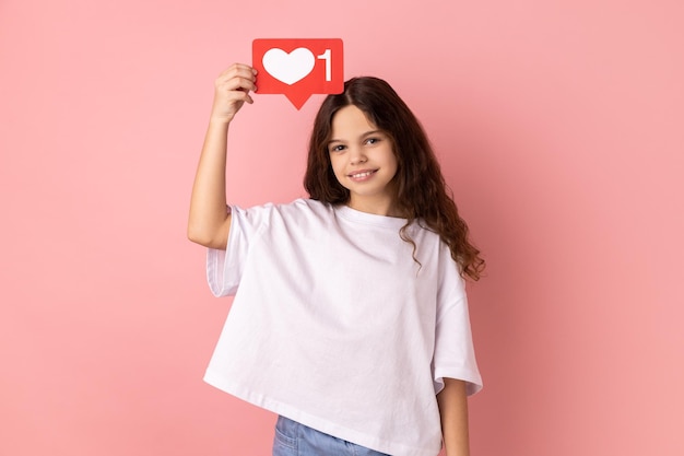 Smiling little girl holding social media heart Like icon above head recommending to follow