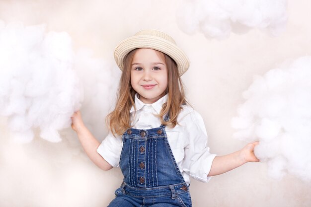 Фото Улыбающаяся маленькая девочка в соломенной шляпе позирует с облаками