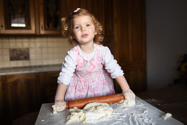 Smiling little girl kneading the dough