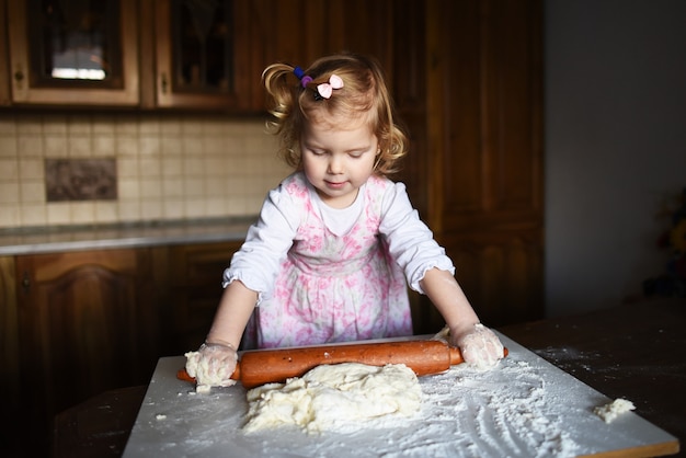 Smiling little girl kneading the dough