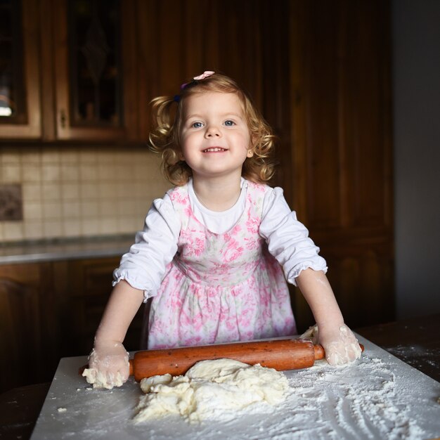 Фото Улыбающаяся маленькая девочка замешивает тесто