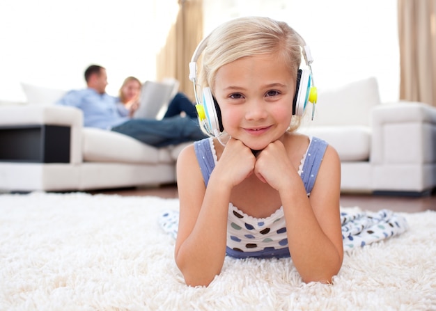 Smiling little girl listening music lying on the floor