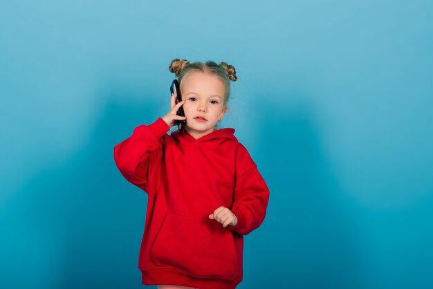 Улыбающаяся маленькая девочка по телефону на синем фоне