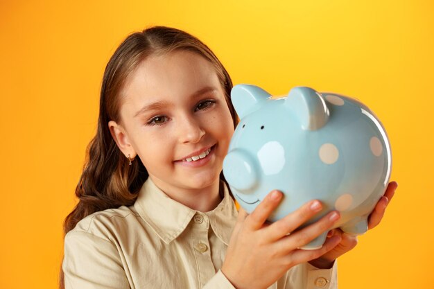 Photo smiling little girl posing with a piggy bank over yellow background