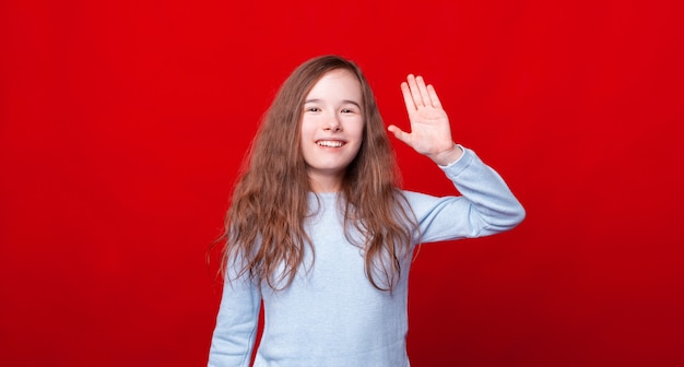 Smiling little girl saying Hello, salute gesture over red wall