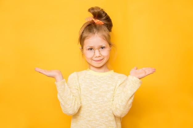 Smiling little girl shows scales on hands on yellow background. Copy space on palms hands