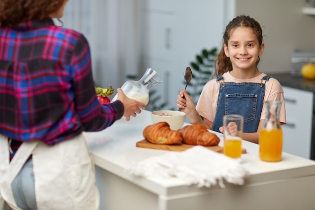 笑顔の少女は、キッチンで母親と一緒に健康的な朝食をとっている親指を示しています。