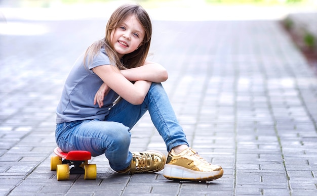 Smiling little girl sits on a skateboard on the street in summer