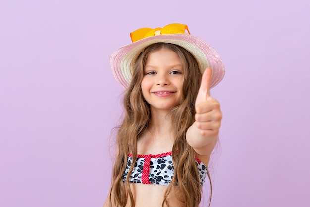 Photo a smiling little girl in a swimsuit on an isolated background gives a thumbs up.