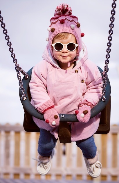 小さな女の子の笑顔、公園のブランコでスイング。女の子は学校や幼稚園の庭で遊ぶ。