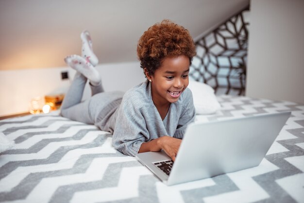 Smiling little girl using laptop in bed.