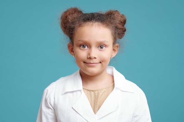 青い背景の上に立っている白いコートで笑顔の少女