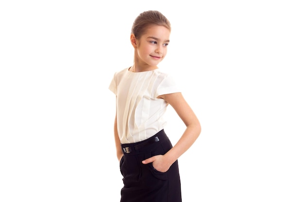Улыбающаяся маленькая девочка с длинным коричневым хвостиком в белой футболке и черной юбке в студии