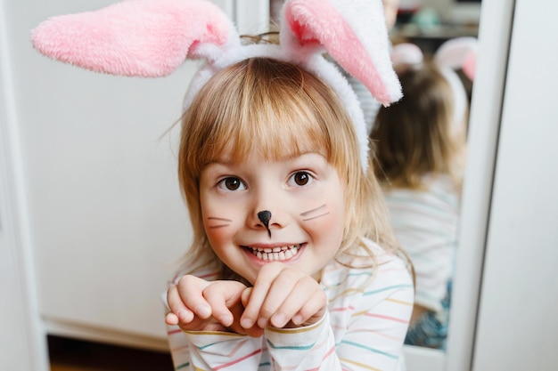 Улыбающаяся девочка с окрашенным лицом и ушами кролика в Пасхальный день