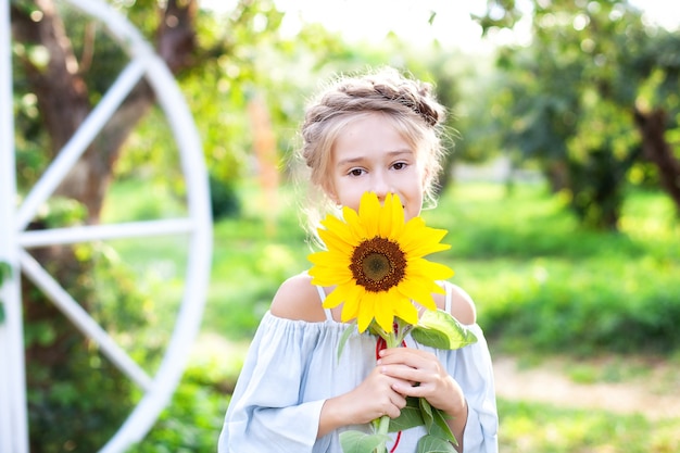 Smiling little girl with a pigtail on her head holds sunflower in garden Child with sunflower