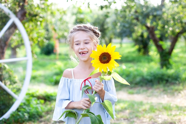 Smiling little girl with a pigtail on her head holds sunflower in garden Child with sunflower