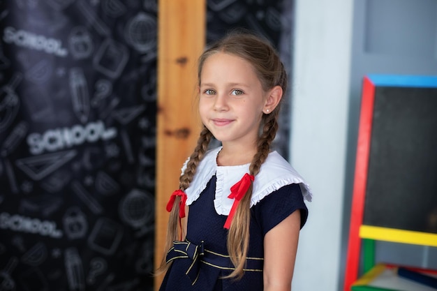 Smiling Little girl with pigtails and in a school uniform stands classroom at school