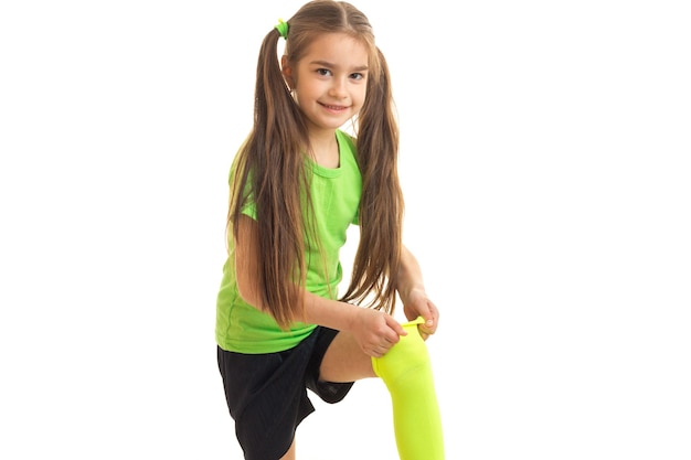 Photo smiling little girl with tails improves sports knee-highs isolated on white background