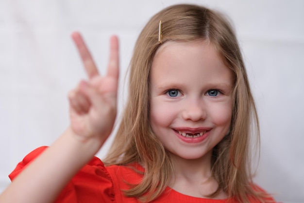 앞니가 없는 웃는 어린 소녀는 긍정적인 유치한 초상화를 두 손가락으로 제스처