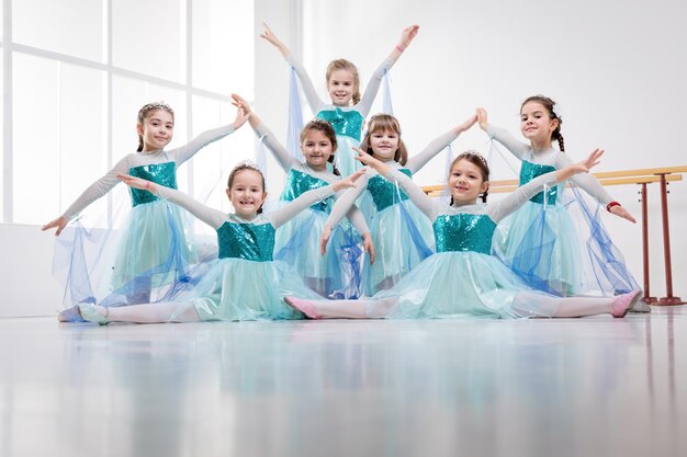 발레 수업 중에 자세를 연습하는 드레스를 입은 웃는 어린 소녀들. 카메라를 찾고 있습니다.
